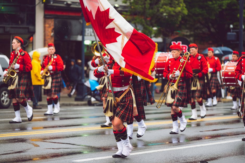Marching band in kilts parades in the rain with Canadian flag on a city street.
