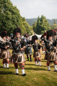 Men in traditional Scottish attire playing bagpipes outdoors during day parade in Scotland.